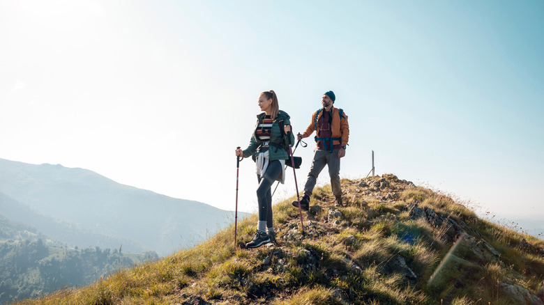 Couple hiking on a scenic mountain trail with backpacks and trekking poles