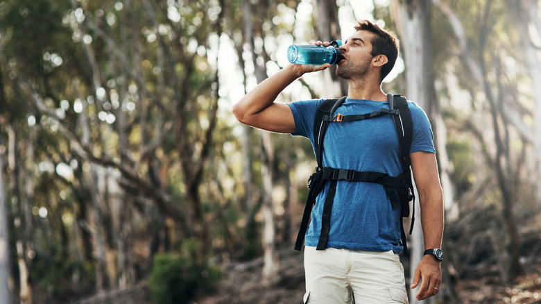 Young man drinking water from a bottle while going for a hike up a mountain