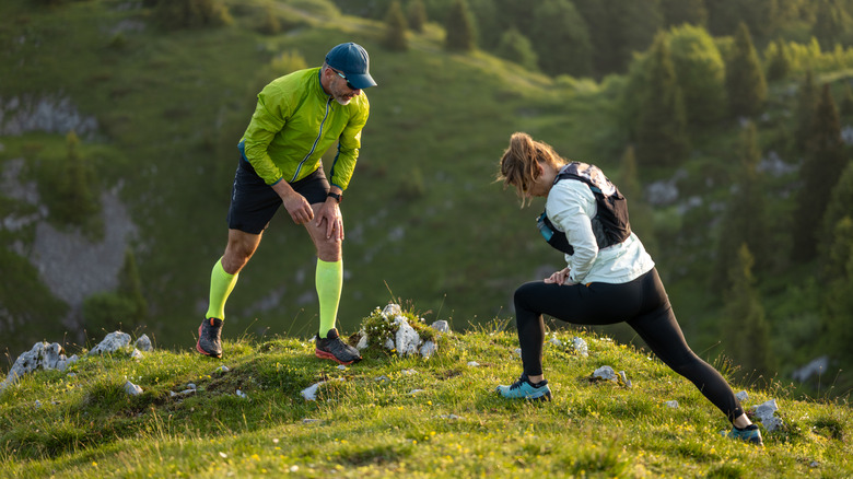 Mature couple stretching together on a grassy hillside