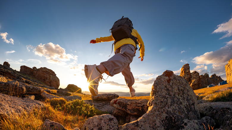 Female hiker jumps from rock to rock on rocky trail at sunset