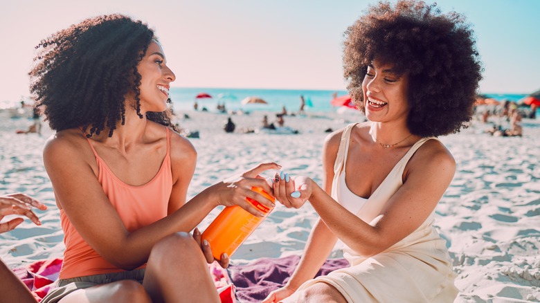 women on beach using sunscreen