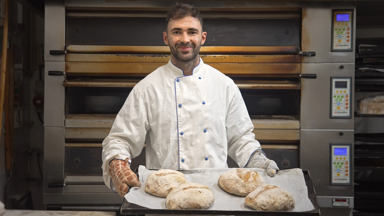 A baker taking freshly-baked bread out of the oven.