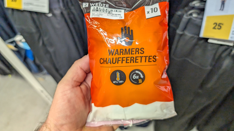 A hand holds out a package of hand warmers.