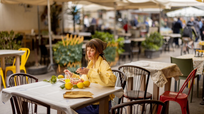 A woman dressed in a yellow shirt dining outdoors alone