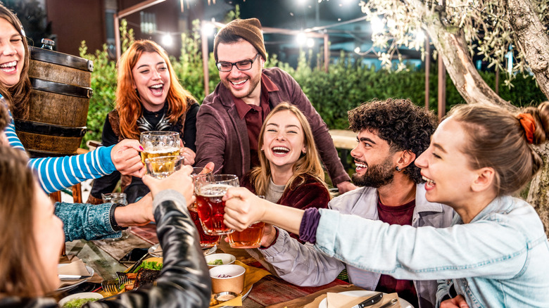 A group of young adults laughing and smiling while holding beer mugs