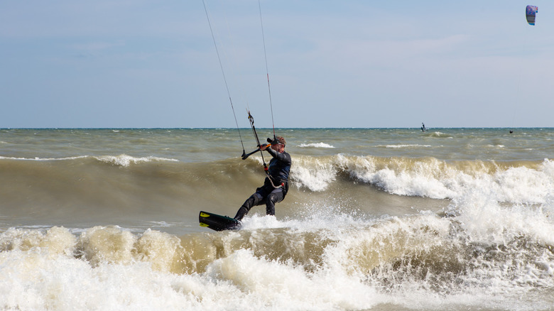 A man in a wetsuit holding onto a kitesurfing bar while gliding over waves.