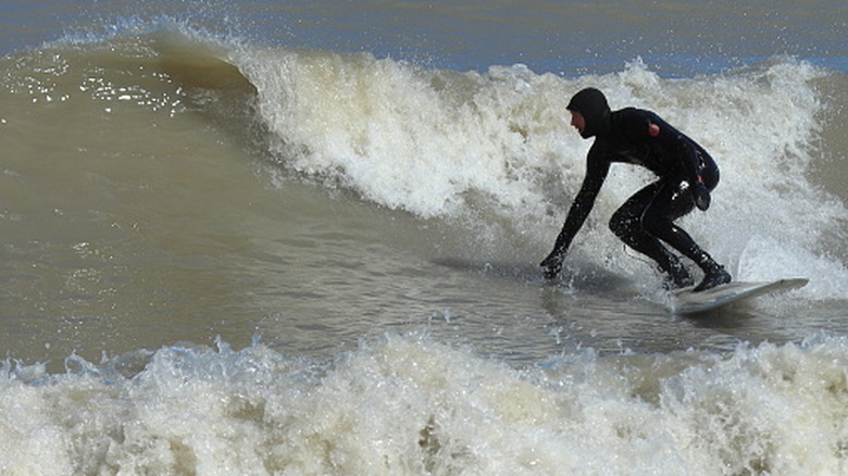 A man surfing while wearing a black wetsuit.