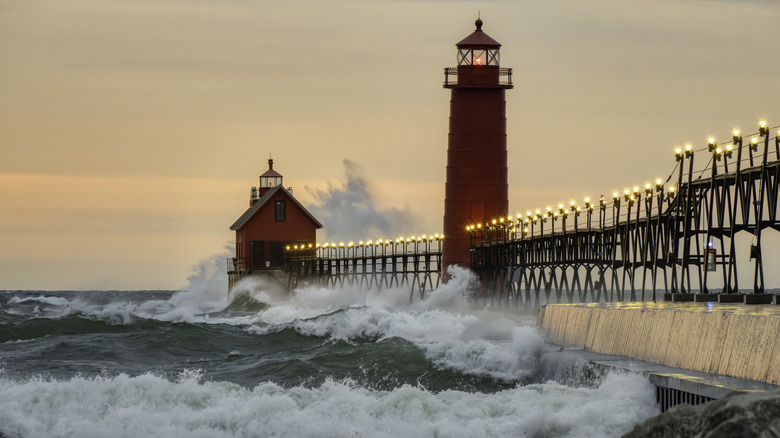 Waves hitting the lit pier with two lighthouses at Grand Haven State Park at dusk.