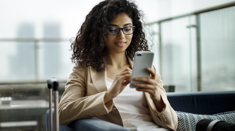 woman checking phone with suitcase next to her