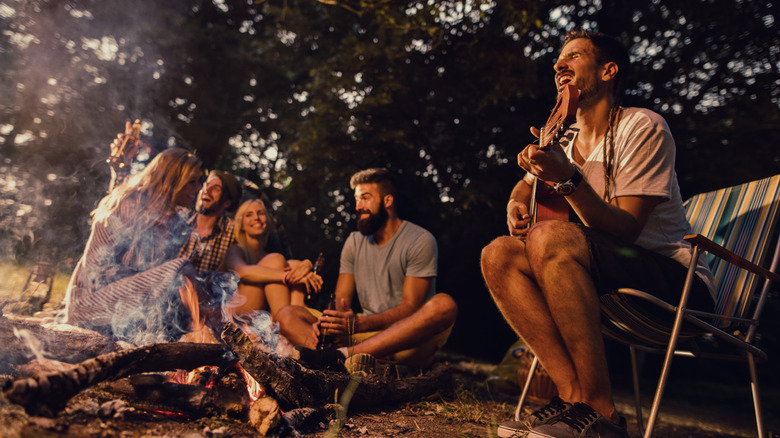A group of youthful campers hangs out around a campfire