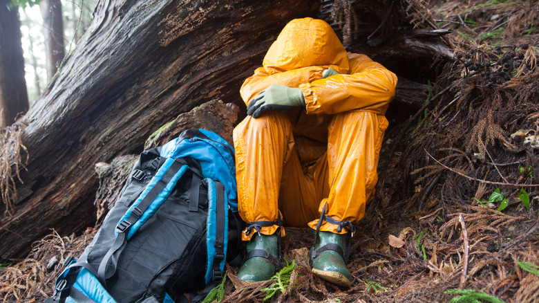 A lost, sad hiker sitting with his head down by a tree