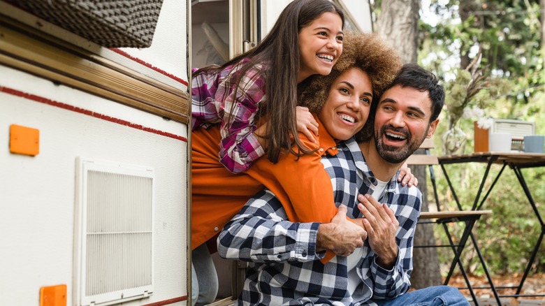 A smiling family of three leans out the door of an RV