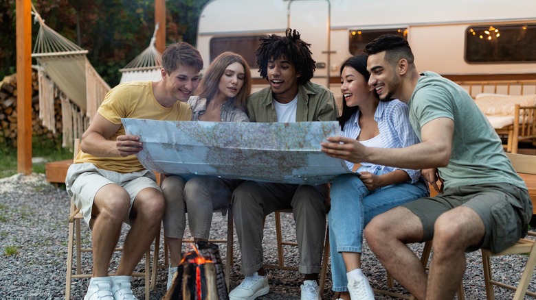 A diverse group of young friends examines a paper map in front of an RV