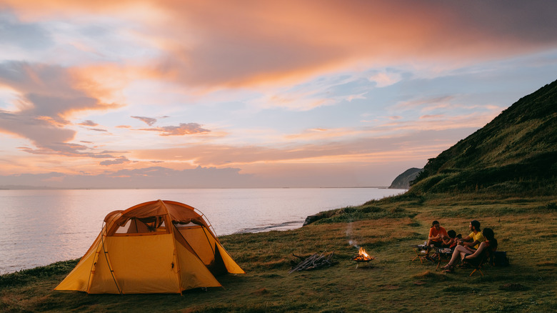campers next to yellow tent and lake at dusk
