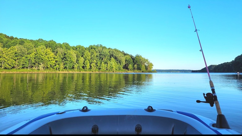 A boat with a fishing pole looking out on a calm lake and forest.