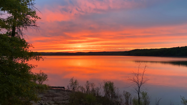 Sunset colors over expansive Monroe Lake in Indiana with hills and trees in the background.