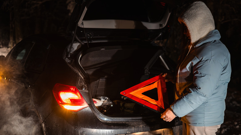 A woman holding a road triangle indicating a broken down car