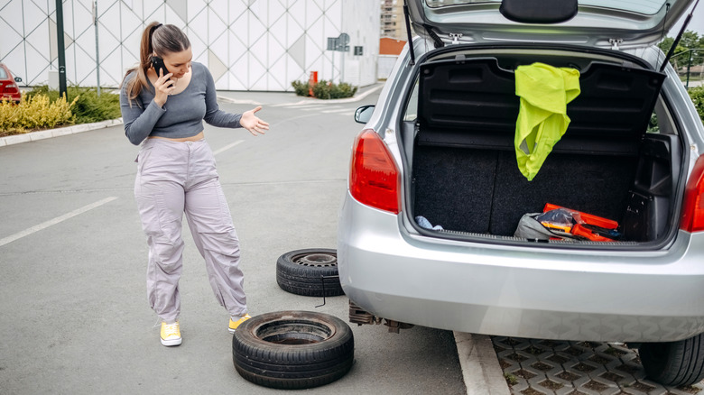 A woman on her phone while changing a car tire