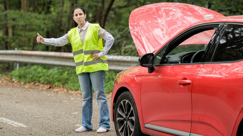 a woman wears the reflective vest for safety next to her broken car