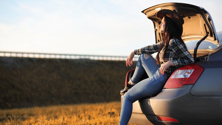A young girl relaxing at the car trunk