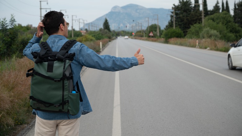 male tourist hitchhiking with backpack along countryside road