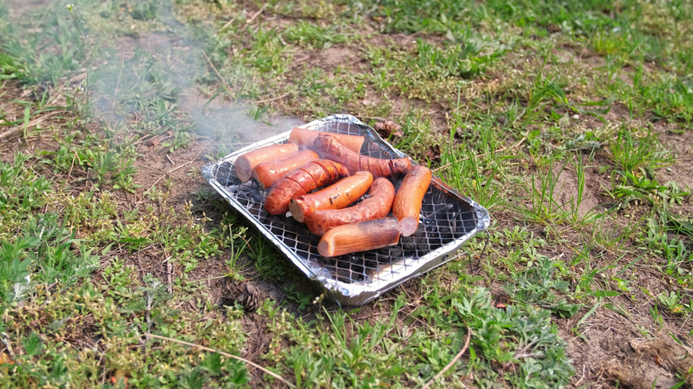 sausages cooking on disposable charcoal grill on grass