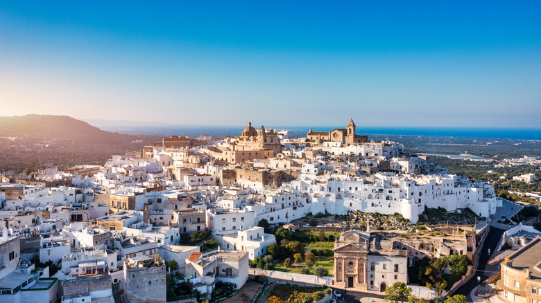 A white Italian village on a hill with a cathedral on top and the sea in the background