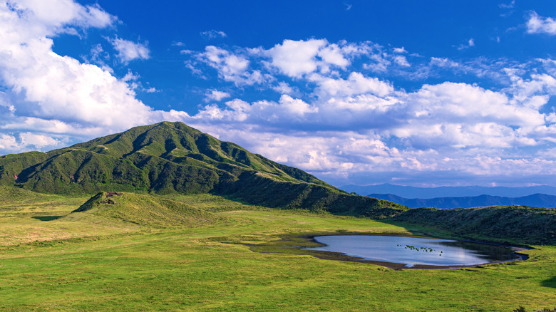 grass covered mountains with a small lake at the base
