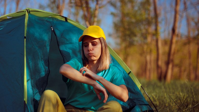 Woman sitting in a tent being bothered by itchy insect bites.