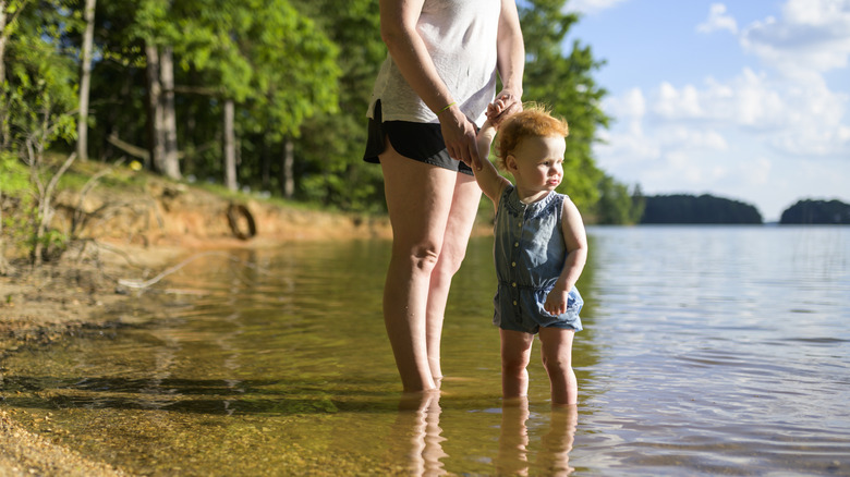 Mother holding a baby's hand on lake shore