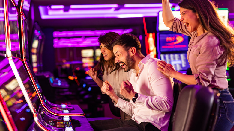 Three people cheery in front of a row of casino slot machines