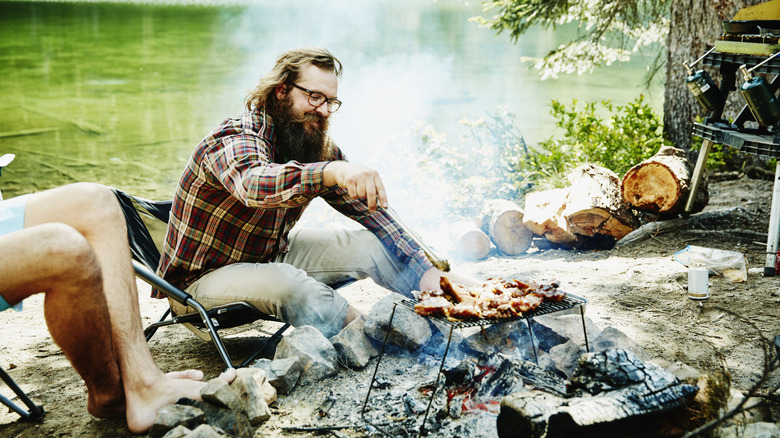 Smiling man with glasses cooking food over campfire