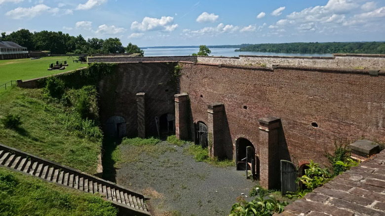 Brick military building with stairs leading from green space and river in the distance