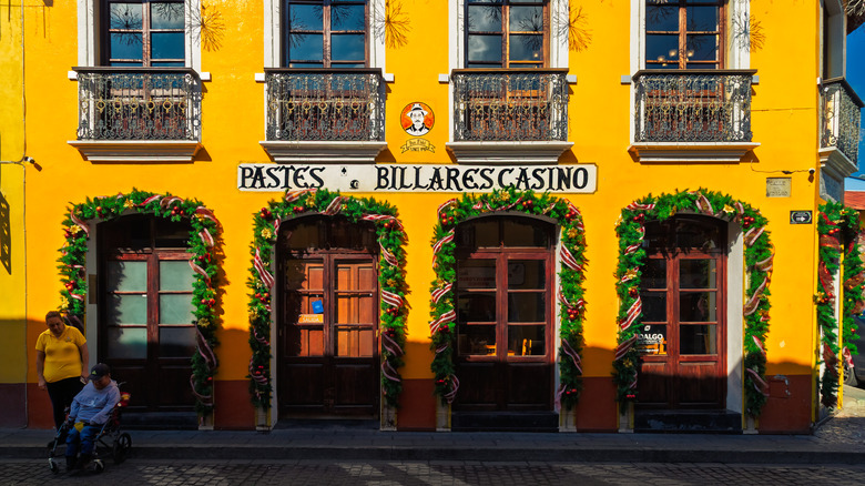 Two people in front of a bright yellow pasty restaurant in downtown Real del Monte