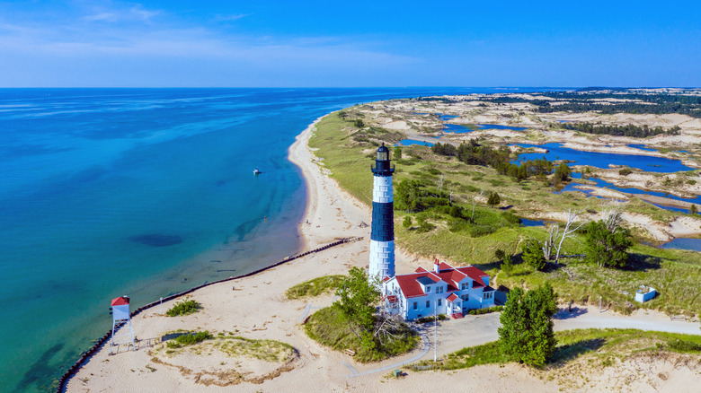 A black and white lighthouse on the beach next to big, blue Lake Michigan