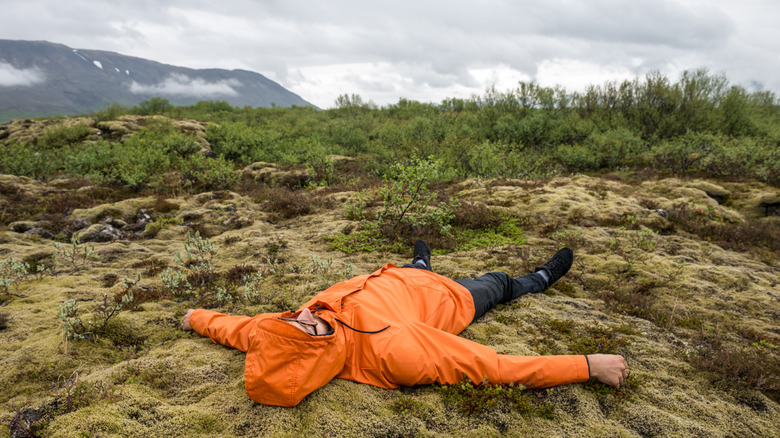 An exhausted hiker lays on their back on a cloudy wet day