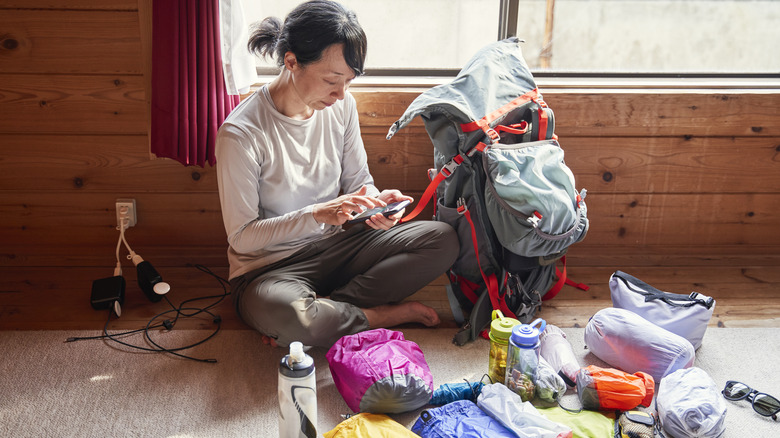 A woman tinkers with her smart phone as she packs a hiker's backpack