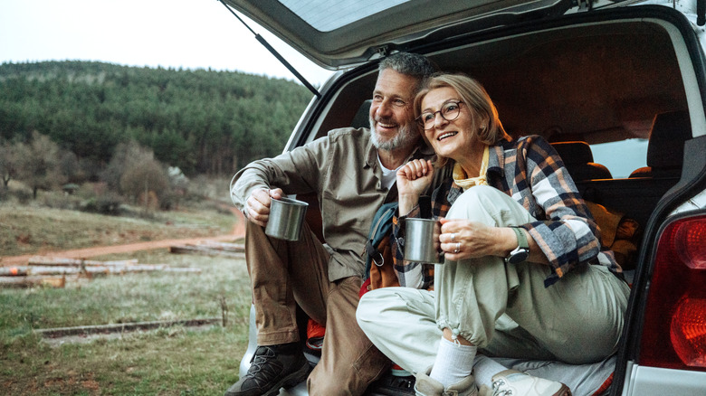 An older couple enjoying coffee in their car's back seat