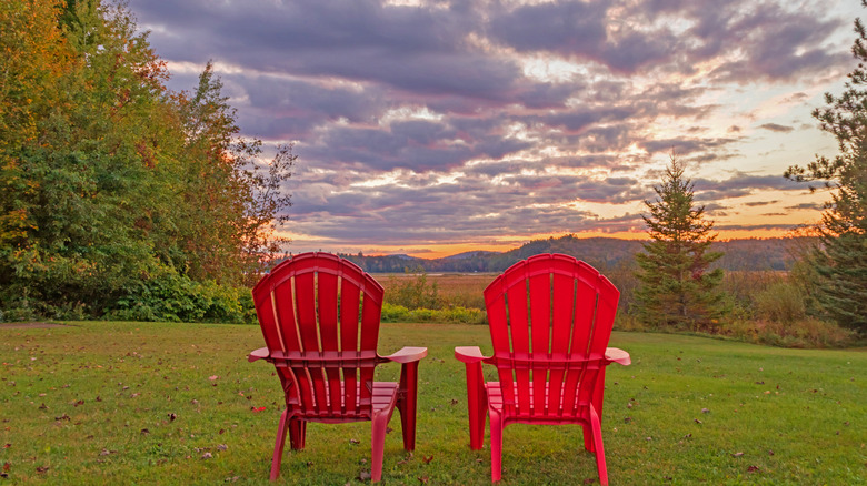 Two red Adirondack chairs facing a scenic sunset