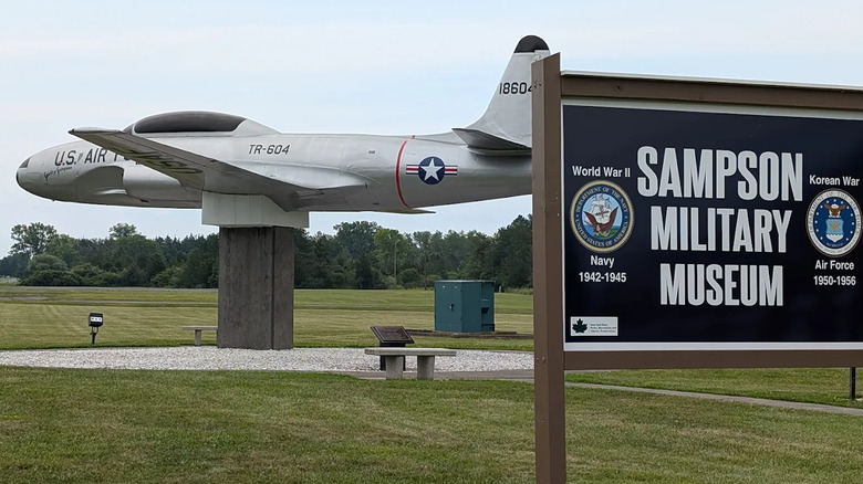 Black sign that reads Sampson Military Museum in front of a gray silver US Air Force aircraft