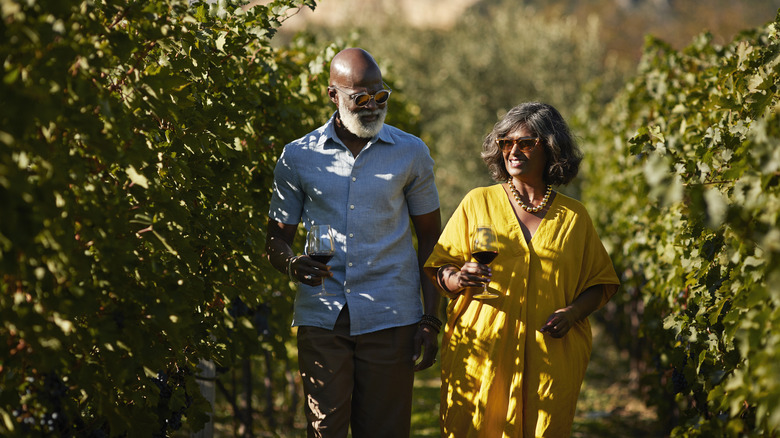Smiling mature woman talking to senior man while walking amidst plants in vineyard