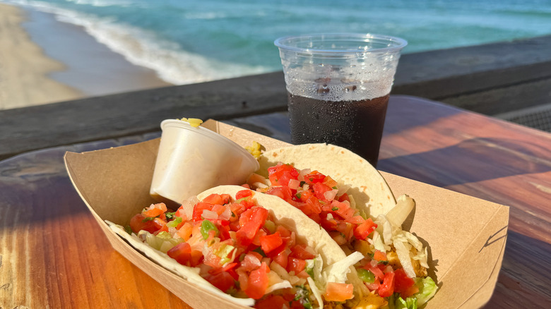 fish tacos and cola on table with ocean in background