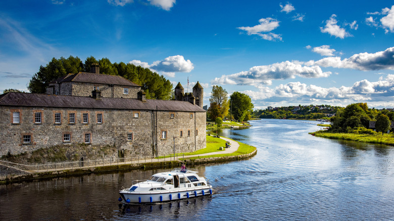 A river cruise boat gently going down the river with an old wall behind it