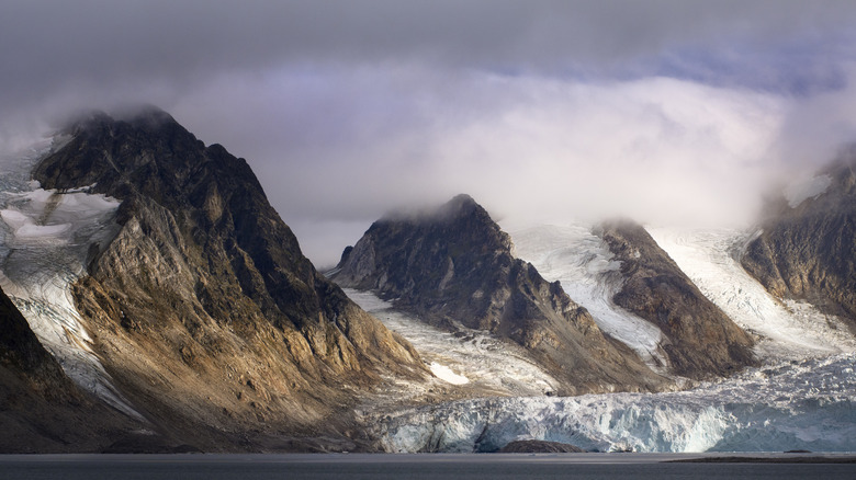 Misty rugged mountains with snow and icebergs in the water