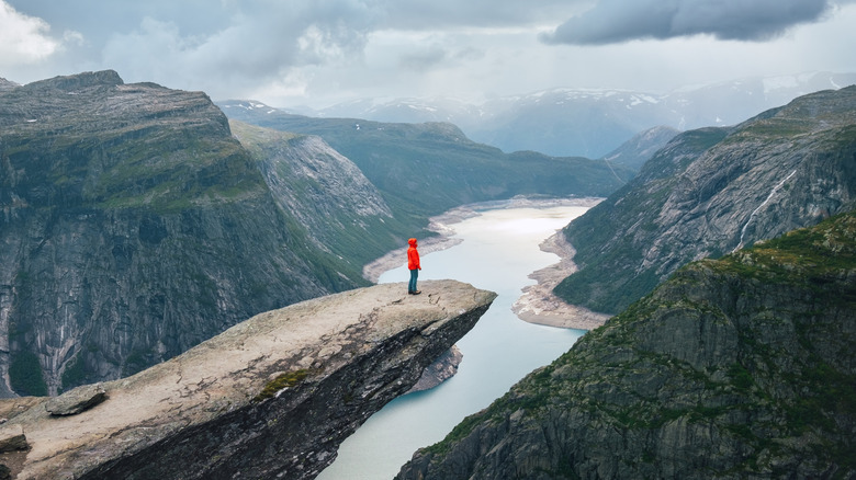 person stands on the edge of Trolltunga rock formation in Norway