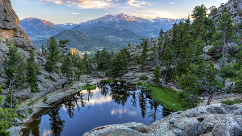 alpine lake in Rocky Mountain National Park surrounded by rocks and evergreen trees with mountains in the distance