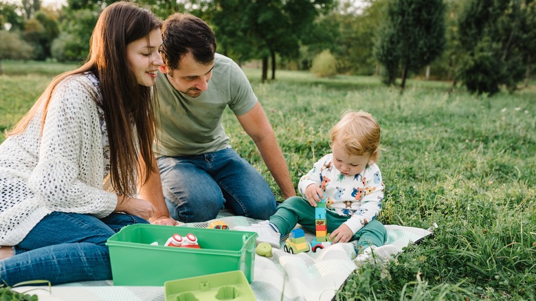 Parents watch their little kid playing with car toys outside