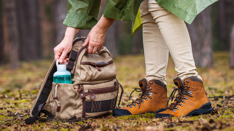 a person wearing hiking boots holding backpack and water bottle