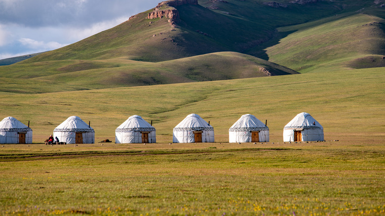 Six white yurts lined in the Kyrgyzstan mountains.