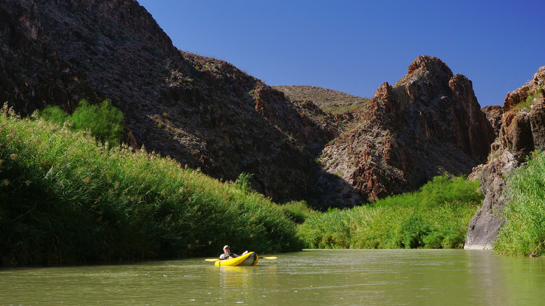 kayaker on a body of water surrounded by green grass and craggy hills, blue sky